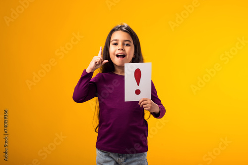 Surprised kid girl holding exclamation point card and pointing finger up. Children, idea and knowledge concept