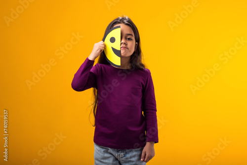 Sad kid girl holding happy half face emoticon. Mental health, psychology and children's emotions concept