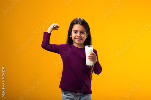 Smiling child girl holding glass of milk and showing strenght gesture. Nutrition and health concept