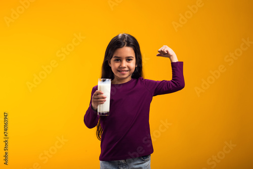 Smiling child girl holding glass of milk and showing strenght gesture. Nutrition and health concept