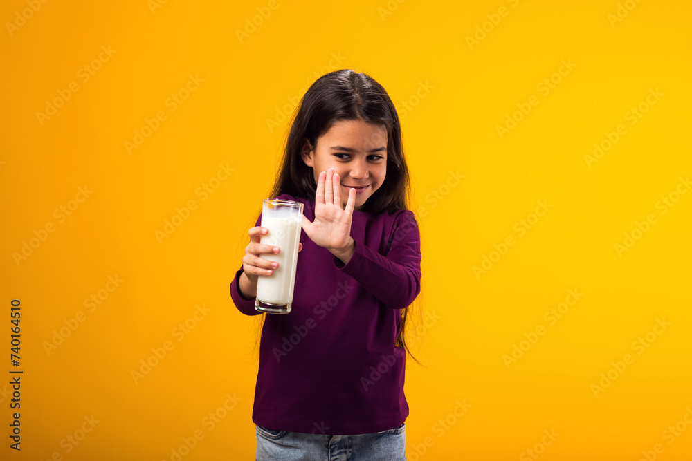 Kid girl with dairy allergy showing stop gesture front glass of milk on yellow background. Lactose intolerance concept Kid girl with dairy allergy showing stop gesture front glass of milk on yellow background. Lactose intolerance concept