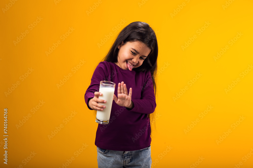 Kid girl with dairy allergy showing stop gesture front glass of milk on yellow background. Lactose intolerance concept Kid girl with dairy allergy showing stop gesture front glass of milk on yellow background. Lactose intolerance concept