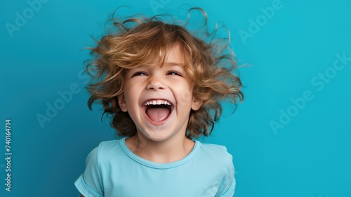 A cute little boy, smiling, stands on a blue background. A happy child, the concept of joy, surprise.