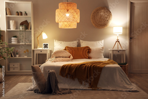 Interior of cozy bedroom with comfortable bed, blanket and glowing lamps at night photo