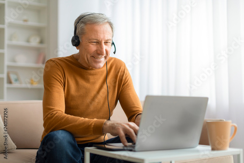 Happy senior man with headset using laptop at home