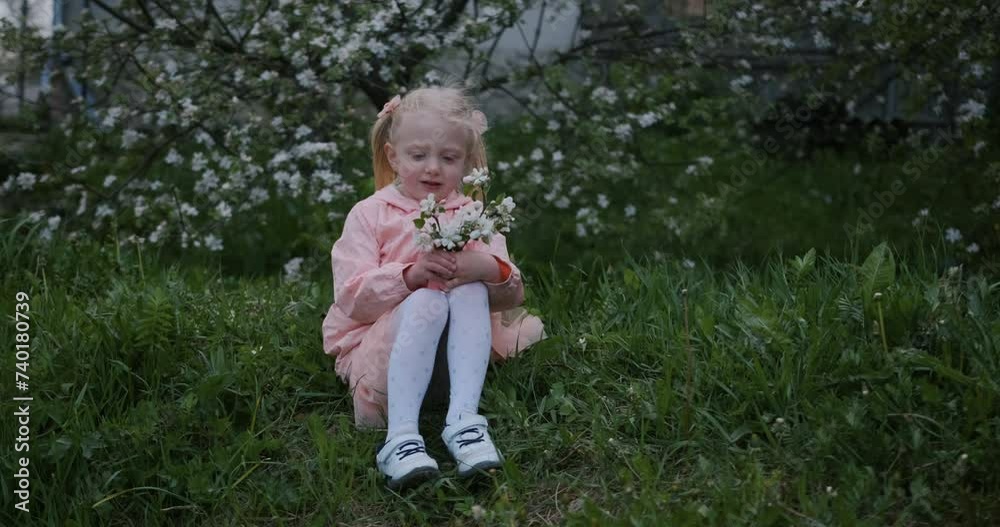 Little girl in pink dress with a bouquet of flowers sitting on the grass Little girl in pink dress with a bouquet of flowers sitting on the grass