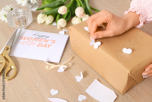 Woman packing gift box for International Women's Day at wooden table, closeup