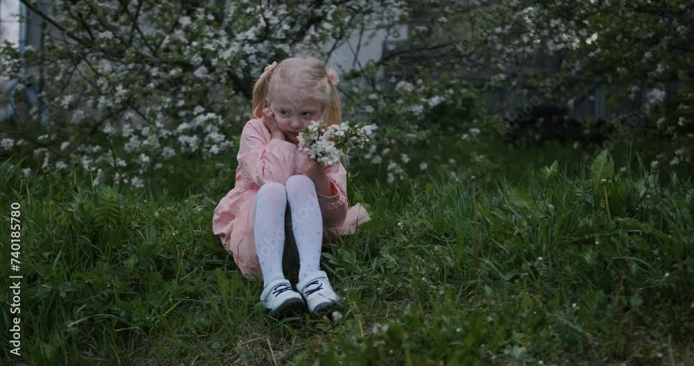 Sad upset little blonde girl sitting alone on the grass in garden. Unhappy child feeling anxious and insecure. Sad upset little blonde girl sitting alone on the grass in garden. Unhappy child feeling anxious and insecure.