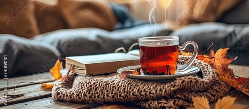 An autumn hygge scene featuring a cup of hot tea and a book resting on a table in a cozy home setting.