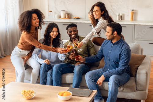 Happy multicultural young people clinking in living room celebrating occasion