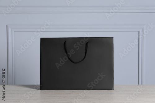 Black paper bag on wooden table against light grey wall