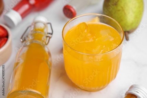 Tasty kombucha in glass and bottles on white table, closeup