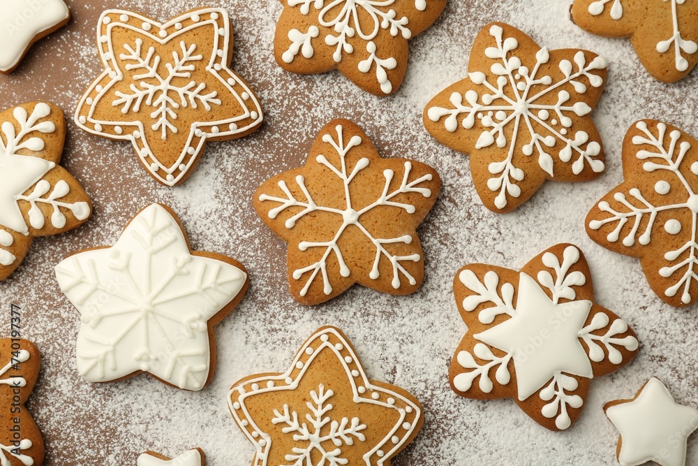 Tasty Christmas cookies with icing and powdered sugar on brown background, flat lay