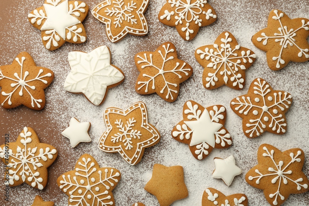 Tasty Christmas cookies with icing and powdered sugar on brown background, flat lay