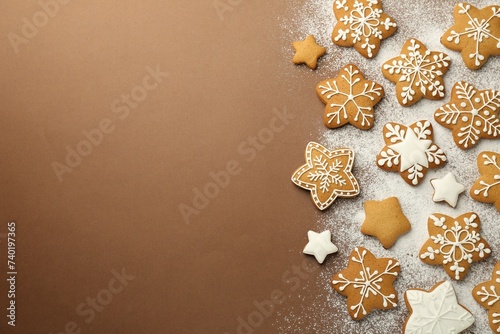 Tasty Christmas cookies with icing and powdered sugar on brown background, flat lay. Space for text