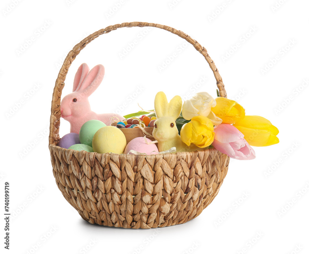 Wicker basket with painted Easter eggs, toy bunnies and tulip flowers on white background