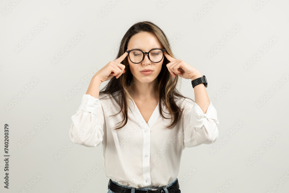 Focused young woman with brown hair wearing glasses and a white blouse holds temples Focused young woman with brown hair wearing glasses and a white blouse holds temples