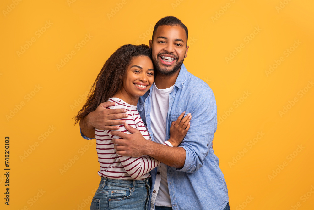 Loving black couple in warm embrace posing against yellow background Loving black couple in warm embrace posing against yellow background