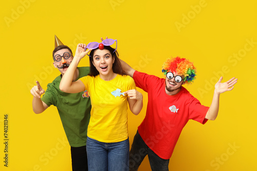 Young surprised friends in funny disguise with paper fishes pointing at viewer on yellow background. April fool's day celebration