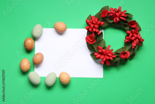 Easter eggs, felt wreath and blank greeting card on green background. Top view