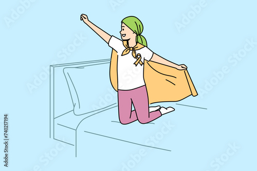 Child with oncology disease stands on bed in superhero pose, for concept day against cancer. Little boy with cancer feels improved mood after defeating deadly disease with chemotherapy