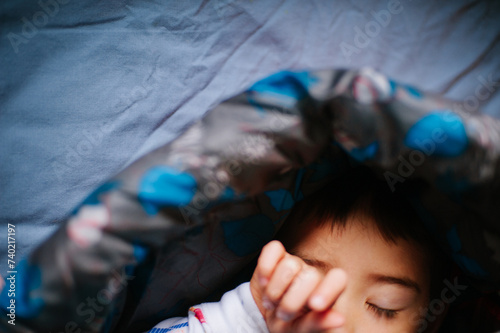 A toddler rubs his eyes as he emerges from his sleeping bag while camping, shallow focus photo