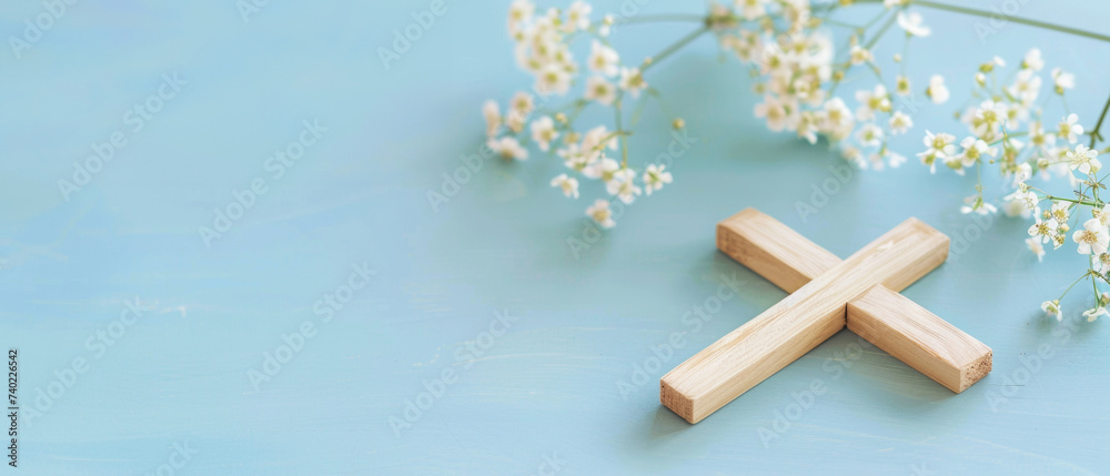 Wooden cross laying next to with spring flowers on blue background. Christianity symbol of Easter, Palm Sunday, Good Friday, Holy Thursday. Religion concept