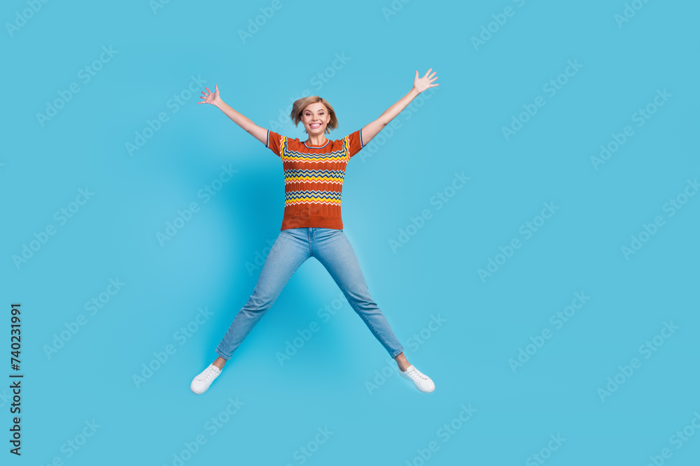 Full size photo of good mood positive woman dressed knit t-shirt denim trousers flying like star isolated on blue color background Full size photo of good mood positive woman dressed knit t-shirt denim trousers flying like star isolated on blue color background