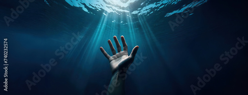 Hand of drowning man under water reaches for the surface. Underwater view of person needs rescue help. Dark deep blue ocean.