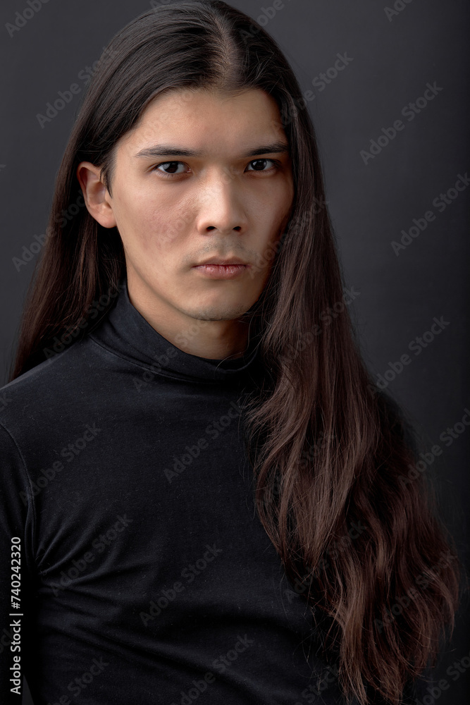Handsome calm man. Trendy young man dressed in black shirt posing in modern studio against dark wall. Portrait of young guy with long straight hair. people, fashion, beauty concept Handsome calm man. Trendy young man dressed in black shirt posing in modern studio against dark wall. Portrait of young guy with long straight hair. people, fashion, beauty concept