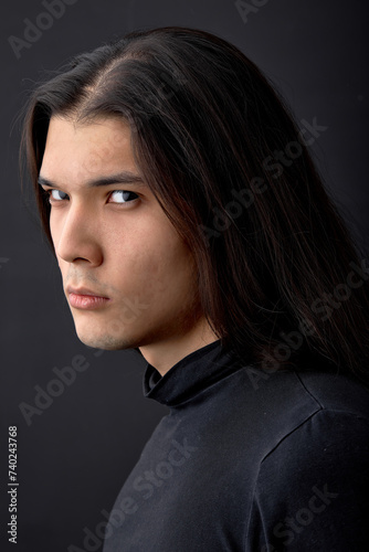 Portrait of hispanic mysterious fashion man with long dark hair and black eyes. unusual male model posing against black studio wall background looking at camera confidently. People and Beauty