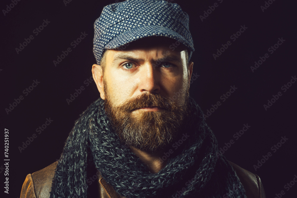 Fashion for men. Attractive bearded man in cap wrapped in gray scarf. Fashionable serious man in trendy leather coat. Closeup portrait of stylish handsome man with beard and mustache in warm clothing. Fashion for men. Attractive bearded man in cap wrapped in gray scarf. Fashionable serious man in trendy leather coat. Closeup portrait of stylish handsome man with beard and mustache in warm clothing.