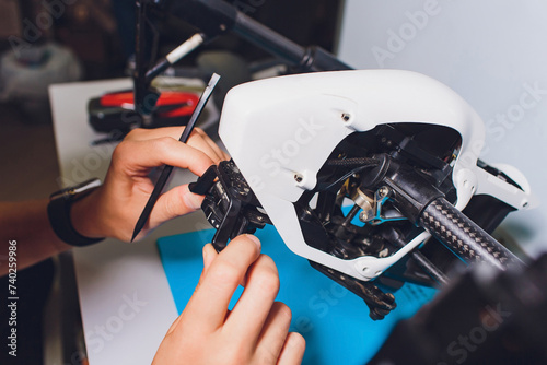 Fototapeta Naklejka Na Ścianę i Meble -  Closeup shot of man working on assembling new surveillance system using quadcopter drone with camera on table with different tools in modern workshop.