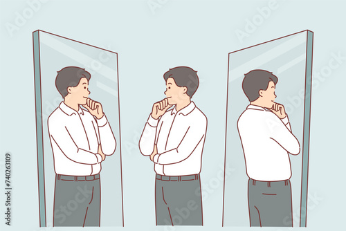 Business man looks in mirror trying on new formal clothes and touches chin with smile