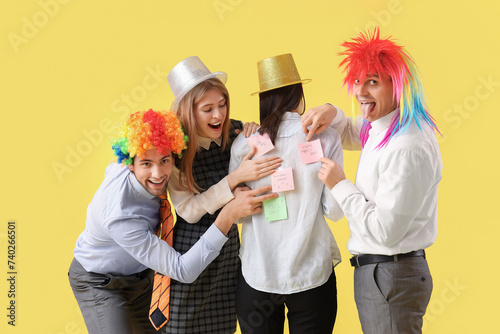 Business people sticking papers on their colleague s back on yellow background. April Fools  Day celebration