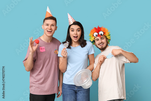 Young friends in funny disguise with paper stickers on blue background. April fool's day celebration