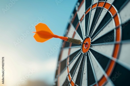 Orange dart arrow hitting bullseye in center target of dartboard on blue sky background with copy space. Business, strategy, achievement, and planning concept photo