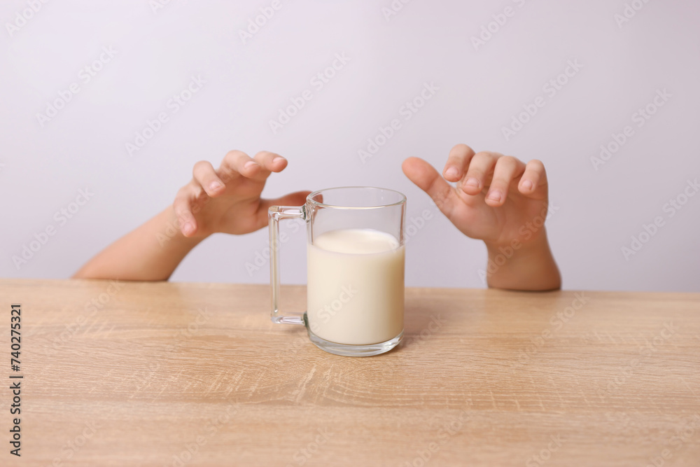 From under the table you can see the child's hands trying to pick up a glass of milk. From under the table you can see the child's hands trying to pick up a glass of milk.