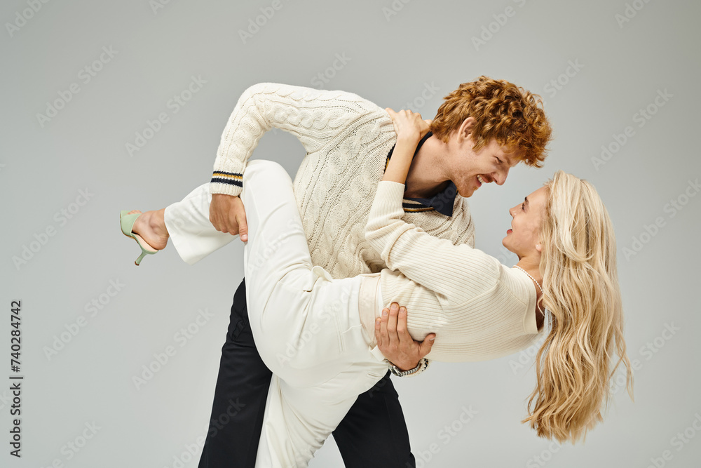 playful redhead man in casual clothes hugging trendy young blonde woman on grey backdrop playful redhead man in casual clothes hugging trendy young blonde woman on grey backdrop