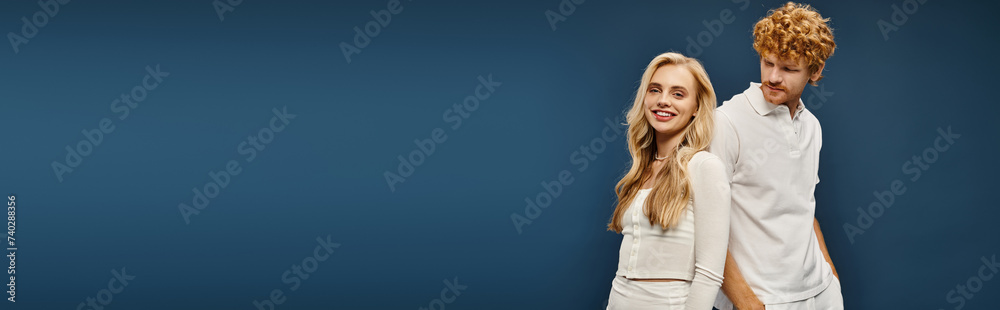 smiling blonde woman in white stylish clothes posing back to back with redhead man on blue, banner smiling blonde woman in white stylish clothes posing back to back with redhead man on blue, banner