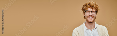 portrait of joyous redhead man in eyeglasses and stylish casual attire on beige backdrop, banner