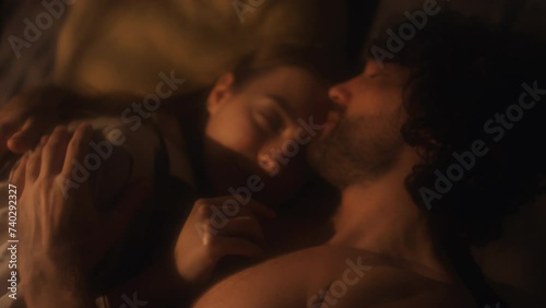 Young affectionate couple kissing and cuddling in bed during night at home