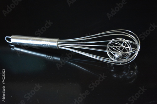 Home furnishings, a metal whisk for whipping egg whites and kneading dough arranged on a black glossy background.