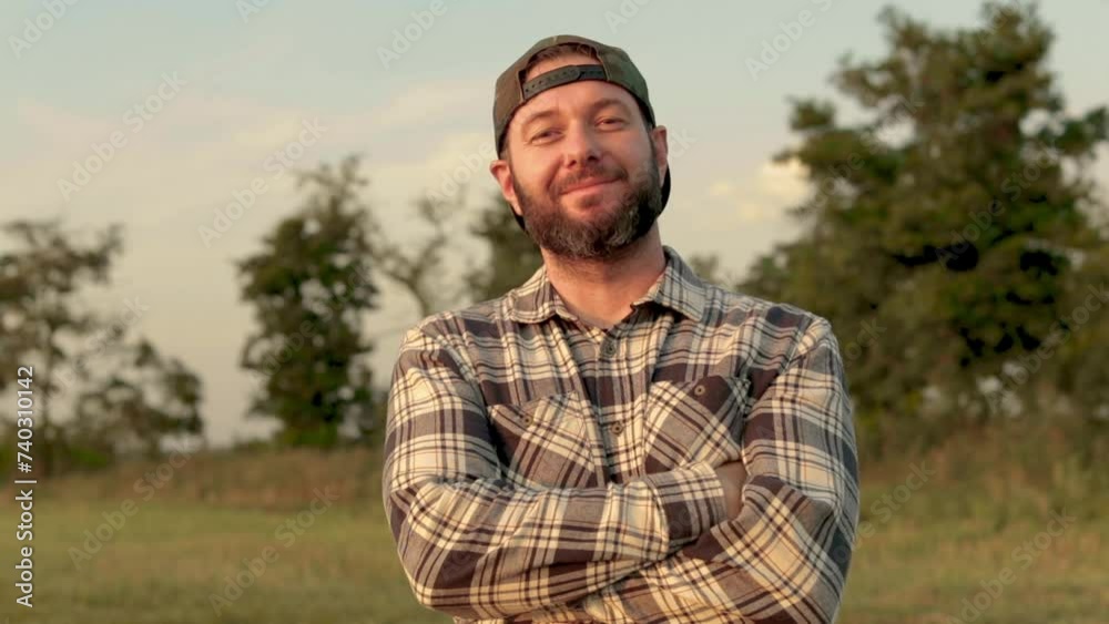 A young bearded farmer puts on a cap. He smiles and looks into the camera. It stands in the middle of an agricultural field. Portrait shooting. A young bearded farmer puts on a cap. He smiles and looks into the camera. It stands in the middle of an agricultural field. Portrait shooting.