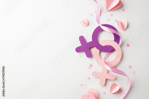 Diversity in unity: the essence of female empowerment. Top view shot of pink and purple female gender symbol surrounded by a swirl of ribbon, hearts, confetti on white background with space for advert photo