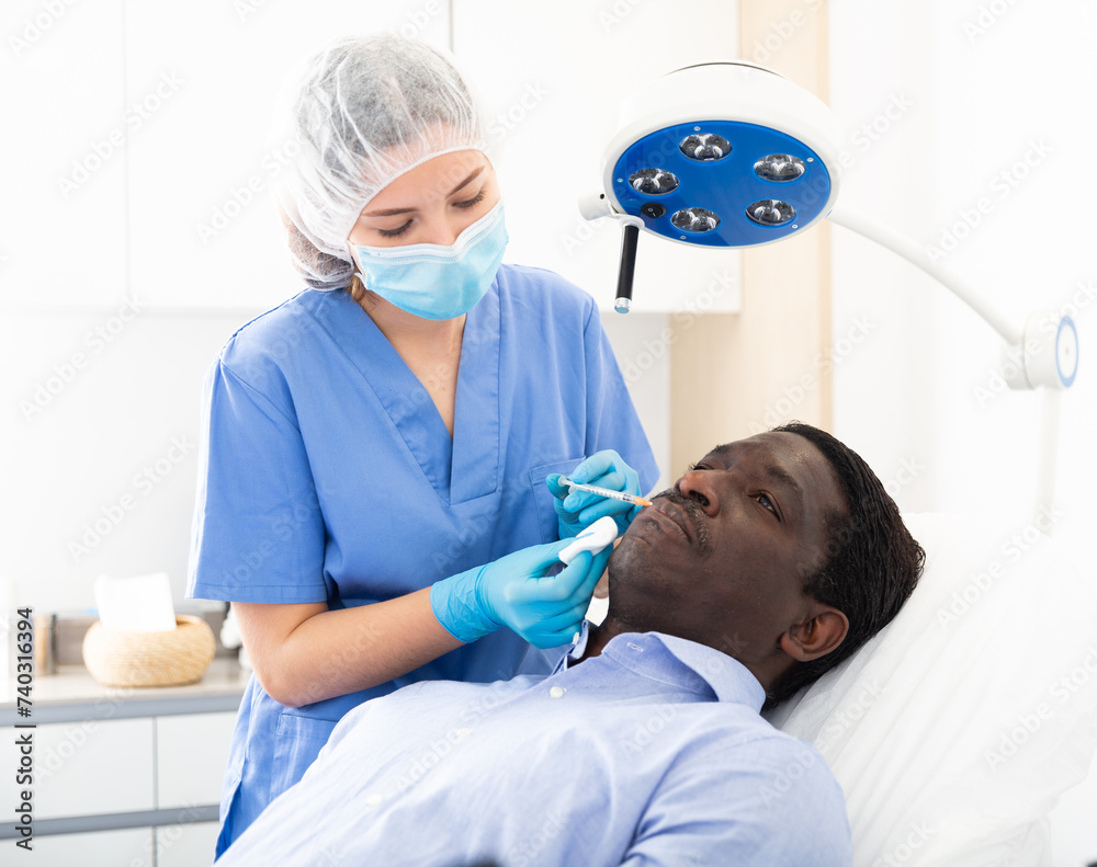 Fototapeta premium Afro american adult man patient of cosmetologist receiving hyaluronic acid injections in aesthetic clinic