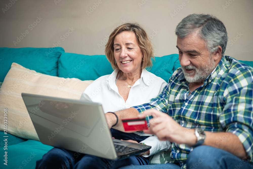 elderly couple with bank card and laptop on sofa elderly couple with bank card and laptop on sofa