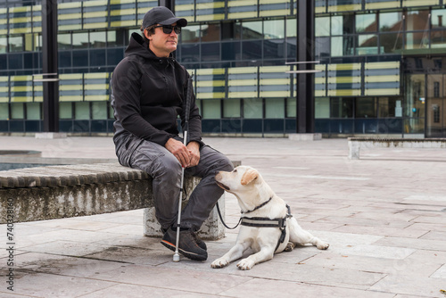Blind man and his guide dog sitting on the street. Visually impaired people and assistance dogs concept.