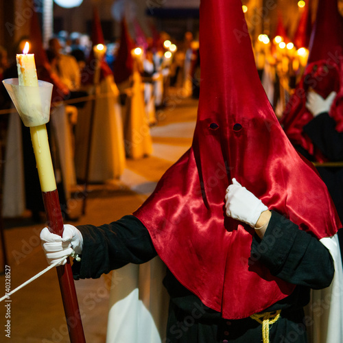 Candle held by unrecognized Member of a brotherhood dressed in tunic and red capirucho in an Holy Week procession at night. Devotee, copy space, nazarene