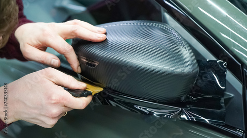 A car wrapping specialist applies a polyurethane film to the car. Selective focus. PPF protective film. The process of installing PPF on the side mirror. Car wrapping close-up. photo